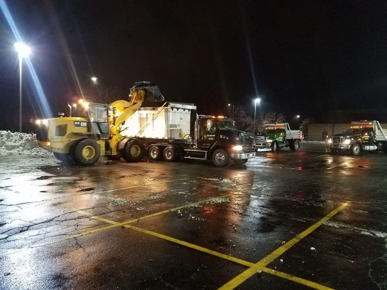 Snow removal equipment clearing a commercial lot at night