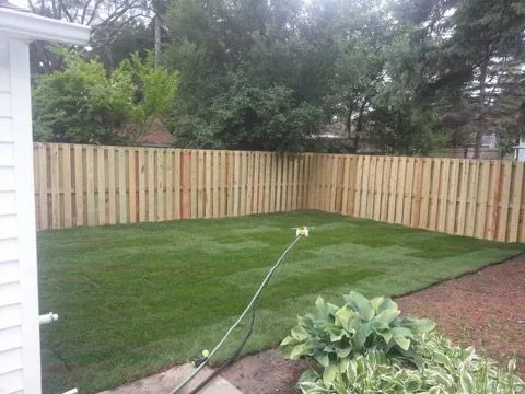 New sod lawn in a fenced backyard with a sprinkler running